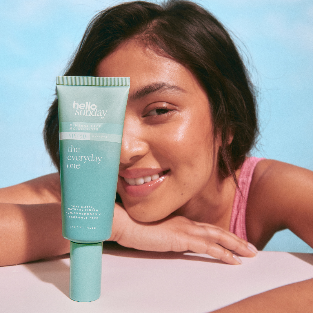 Woman holding a tube of 'hello sunday' sólarvörn against a blue background