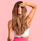 Woman with long blonde hair using a pink hair product against a pink background