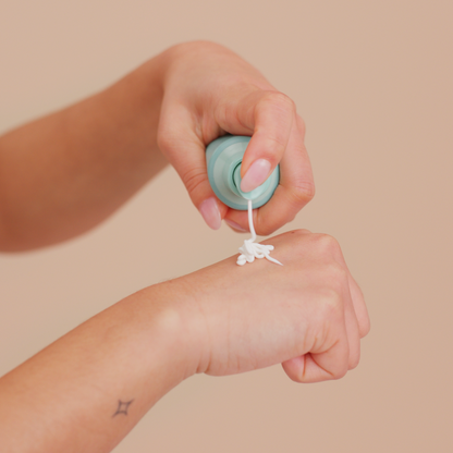 Hand applying a small container of cream to another hand against a beige background