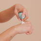 Hand applying a small container of cream to another hand against a beige background