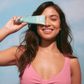 Woman holding a bottle of Hello Sunday mineral sunscreen against a clear blue sky